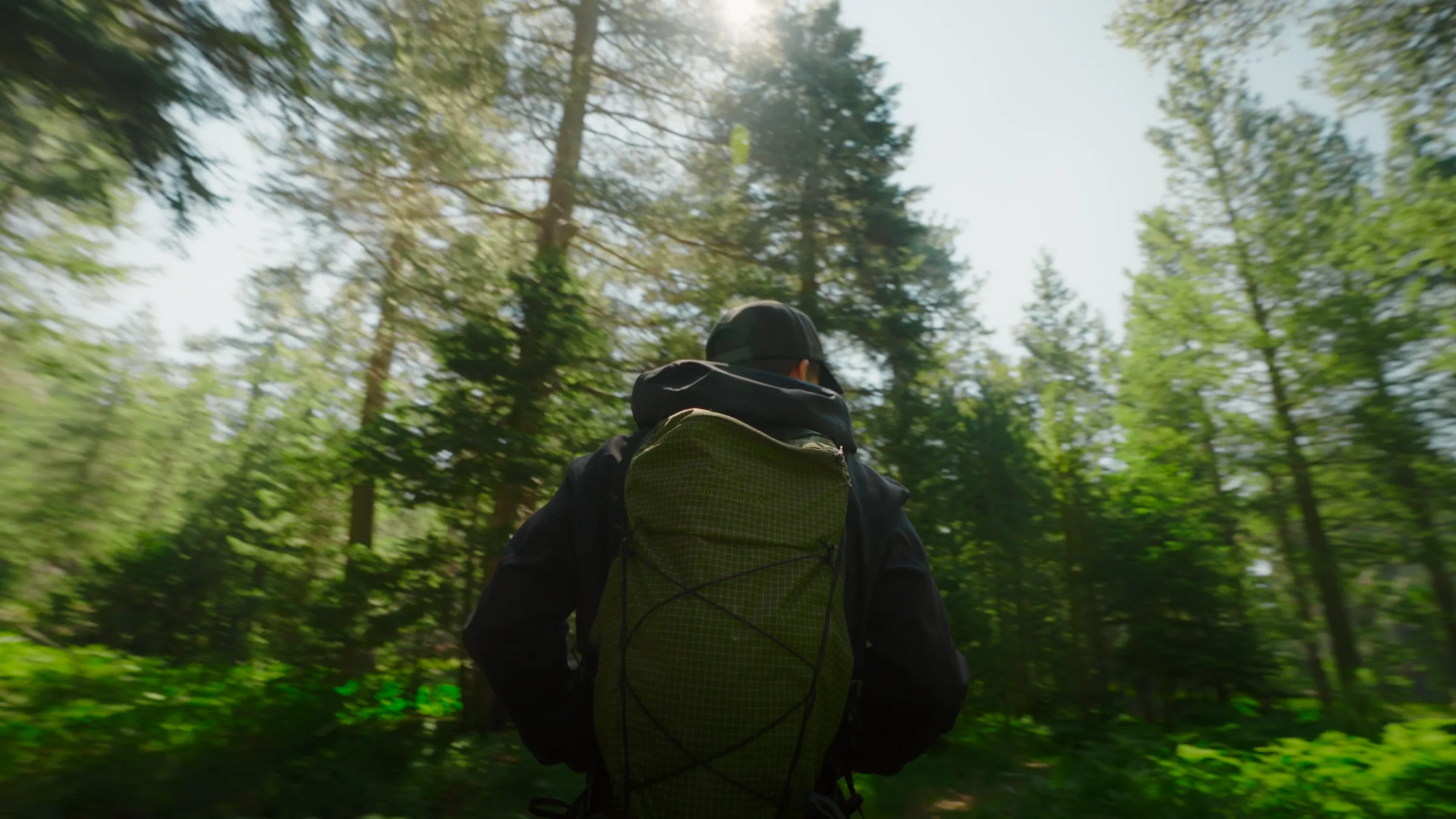 Wide shot of a hiker approaching a log cabin clearing among granite boulders and tall pines