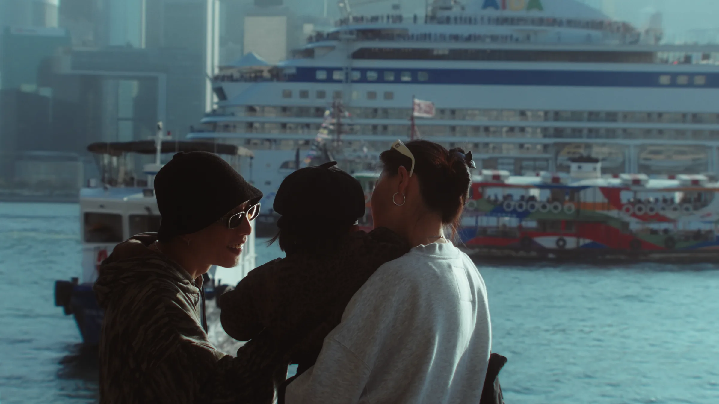Three friends seen from behind at the Hong Kong harbourfront, a cruise ship and a Star Ferry moored across the water